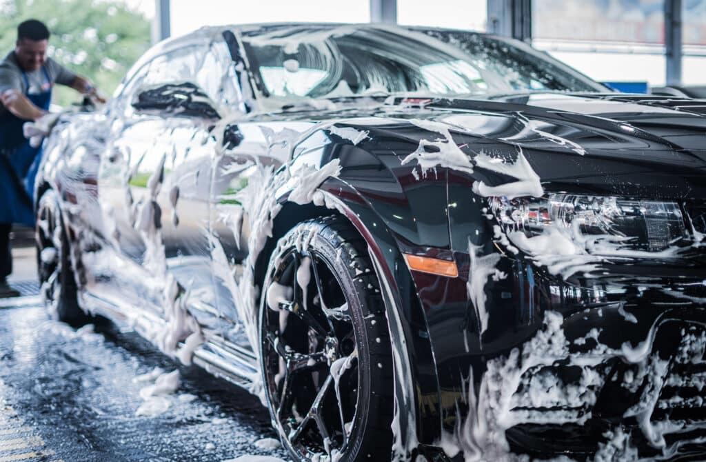 A man diligently washes a black car at a car wash, ensuring it shines brightly and is free of dirt.