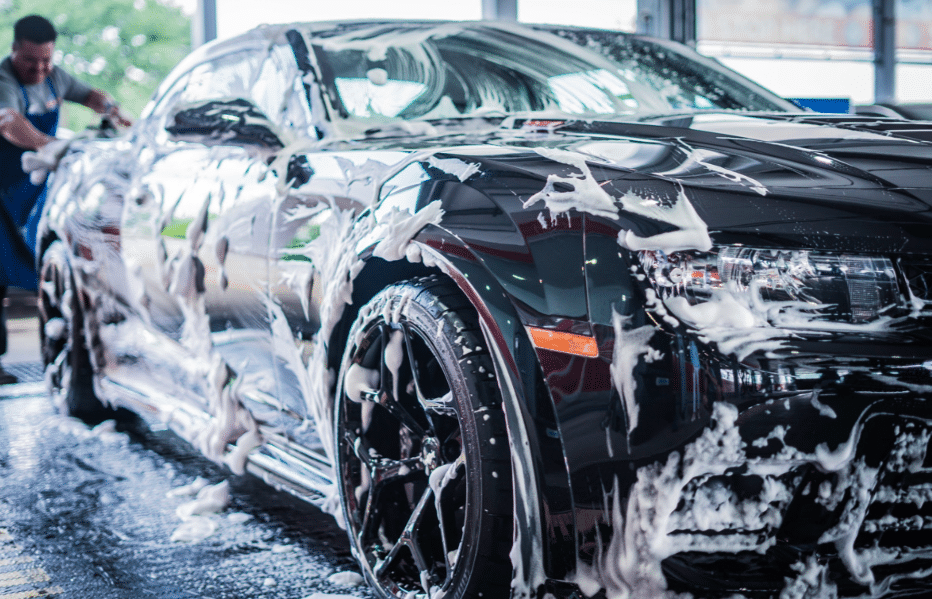 A man diligently washes a black car at a car wash, ensuring it shines brightly and is free of dirt.