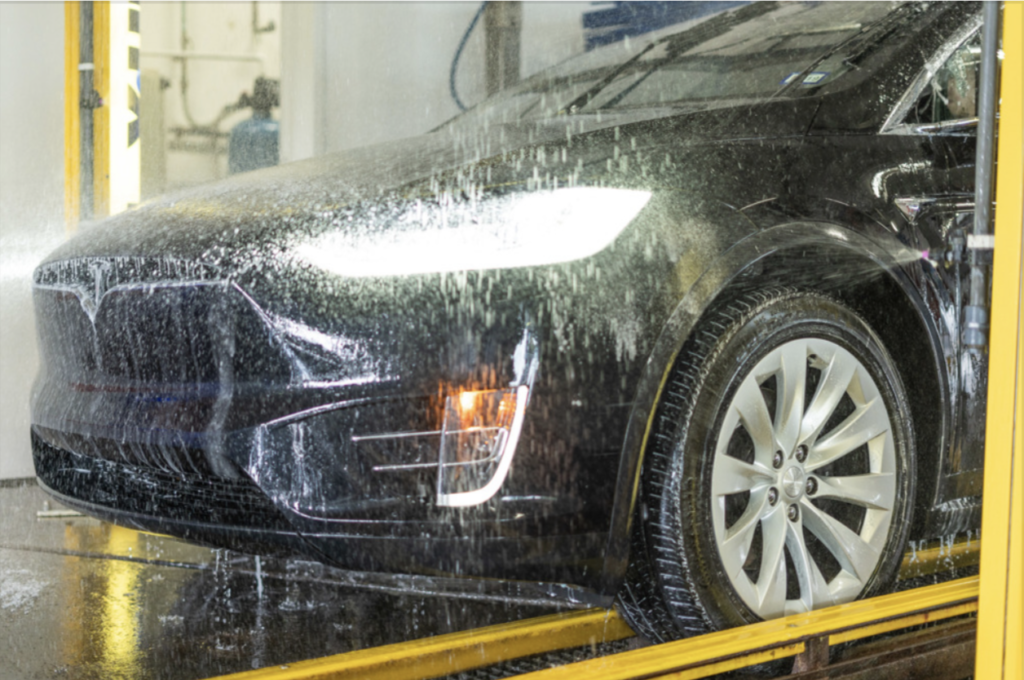 A Tesla car is being thoroughly washed at a modern car wash, showcasing its sleek design and shiny exterior.