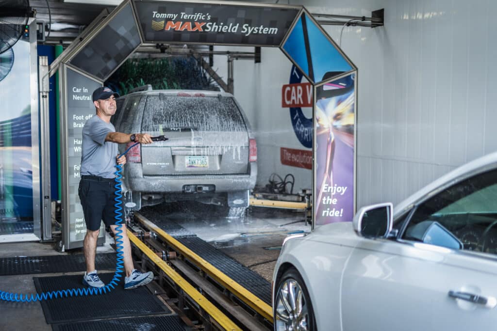 A man diligently washes a car at a car wash, surrounded by soap and water, ensuring a thorough clean.