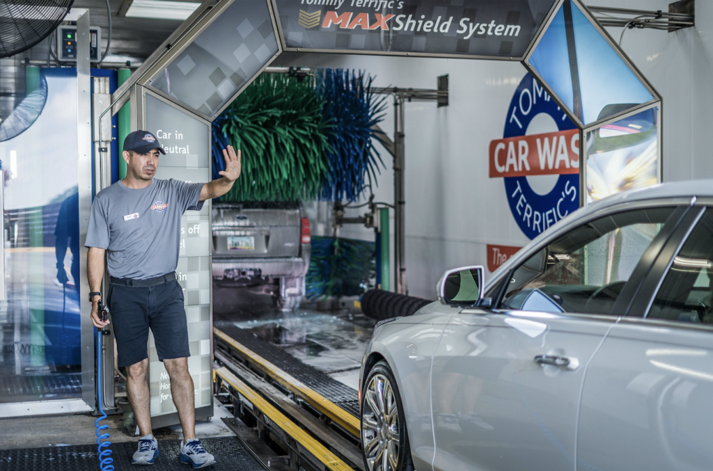 A man diligently washes his car at a car wash, surrounded by soap and water spray.