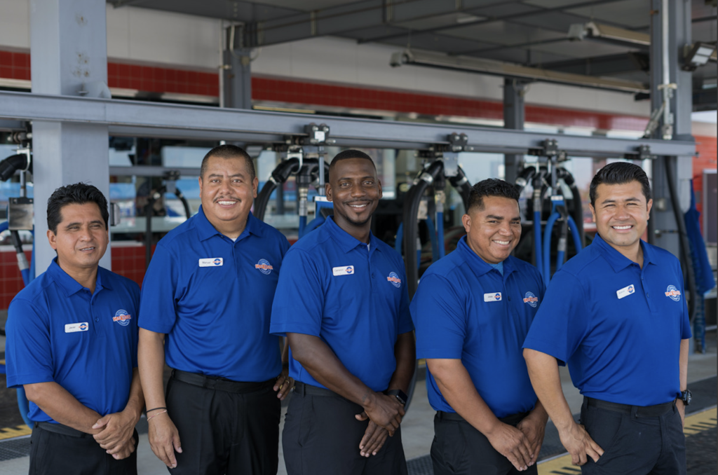 Five men in blue shirts pose together in front of a parked car, showcasing camaraderie and teamwork.