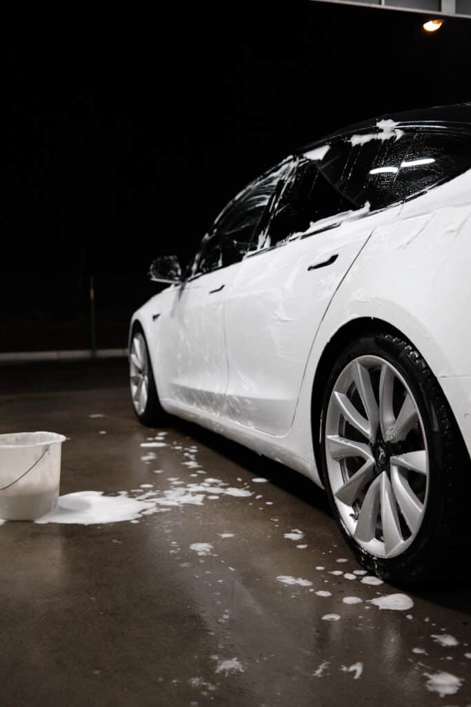 A white Tesla car is being washed inside a garage, showcasing the vehicle's sleek design and cleanliness.