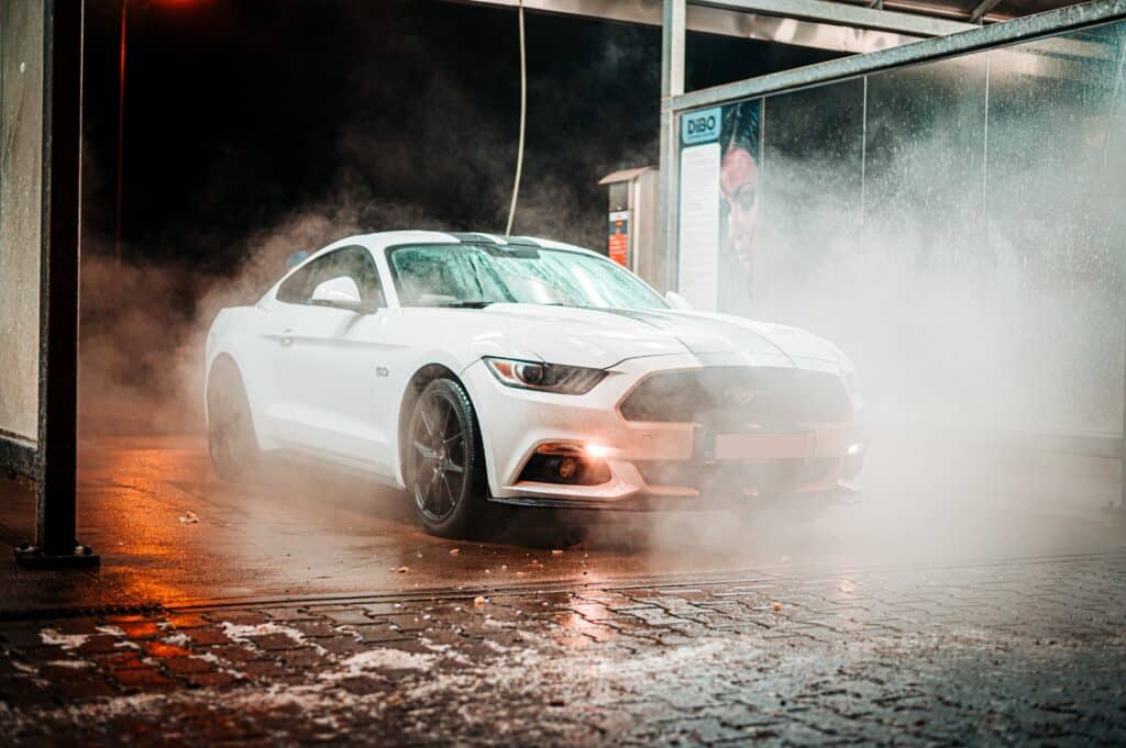 A white Mustang car is being sprayed with water, showcasing its sleek design and shiny exterior.