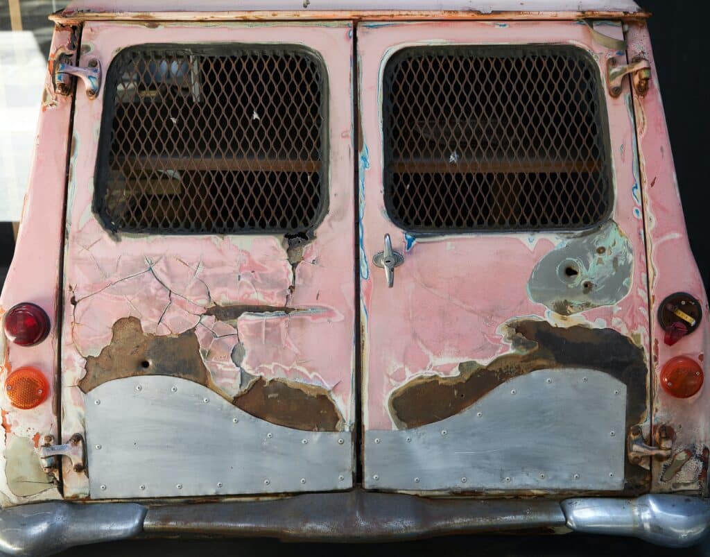 An old, rusted van with a broken door and shattered window, showcasing years of neglect and decay.