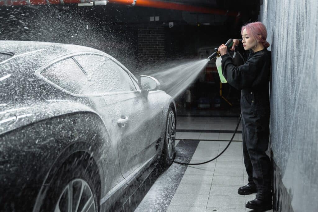 A woman diligently washes a car inside a garage, showcasing her attention to detail and care for the vehicle.