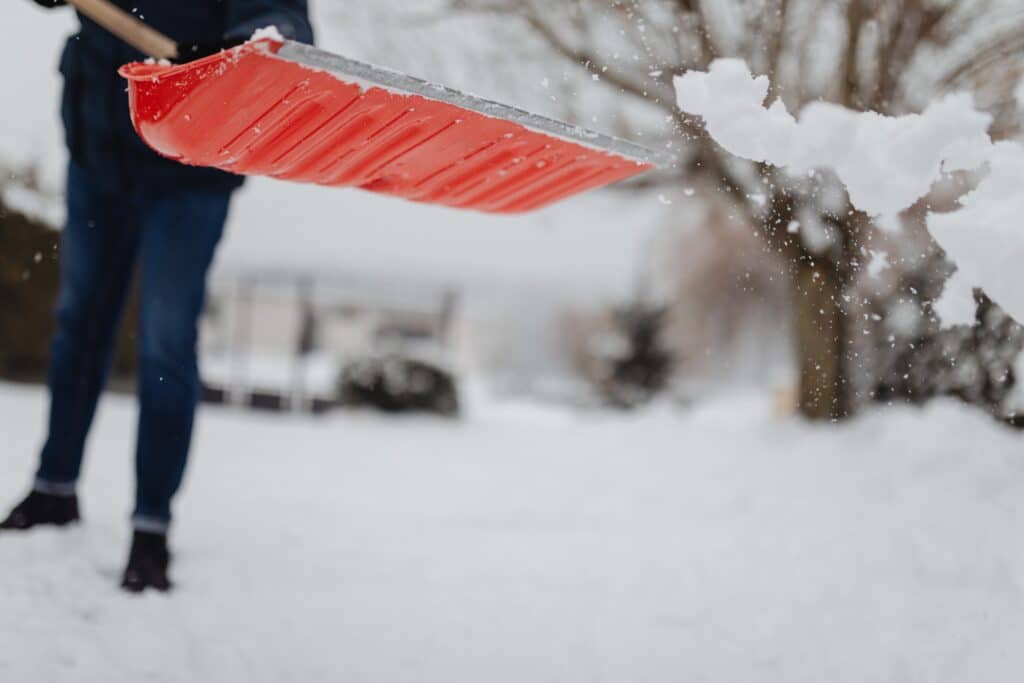 A person shoveling snow from the ground, clearing a path in a winter landscape.