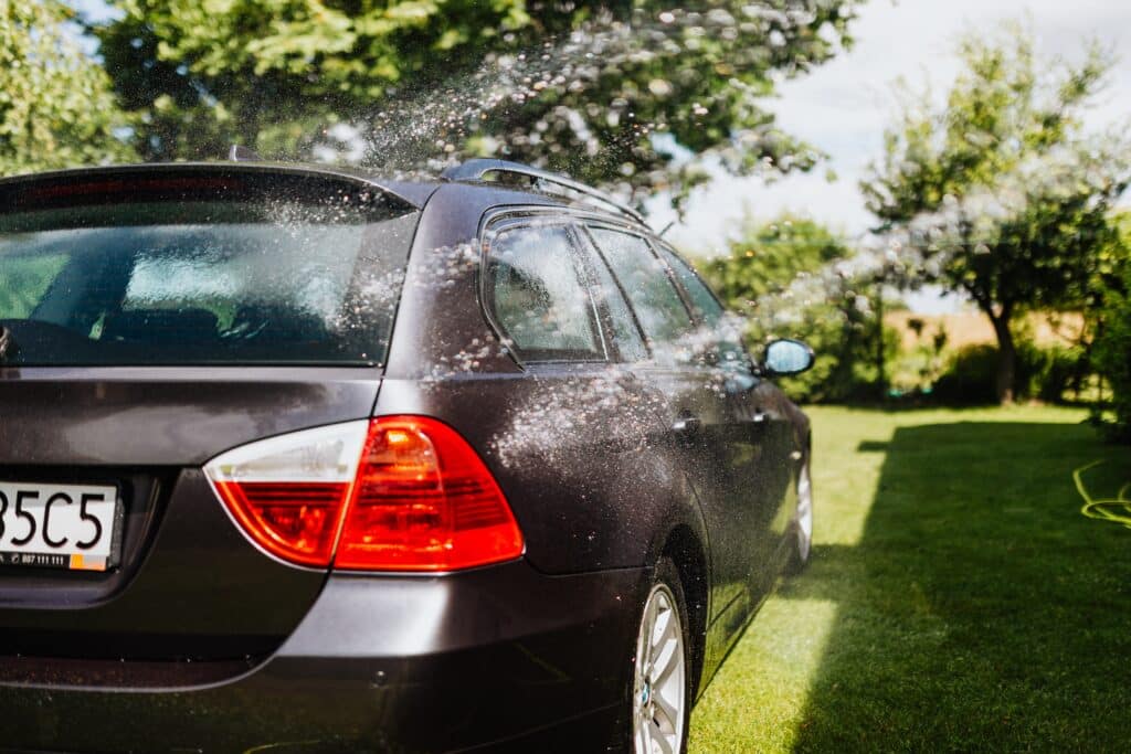 A car sprays water onto the grass, creating a refreshing mist in a sunny outdoor setting.