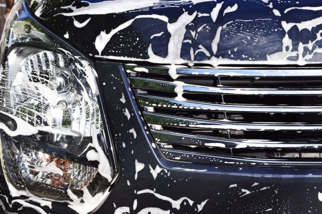 A car enveloped in thick foam during a wash, showcasing a clean and shiny exterior beneath the suds.