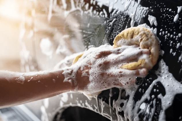 A person scrubbing a car with soap and water, ensuring a clean and shiny exterior.