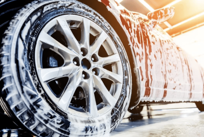 A car is being thoroughly cleaned at a car wash, with water and soap spraying over its surface.