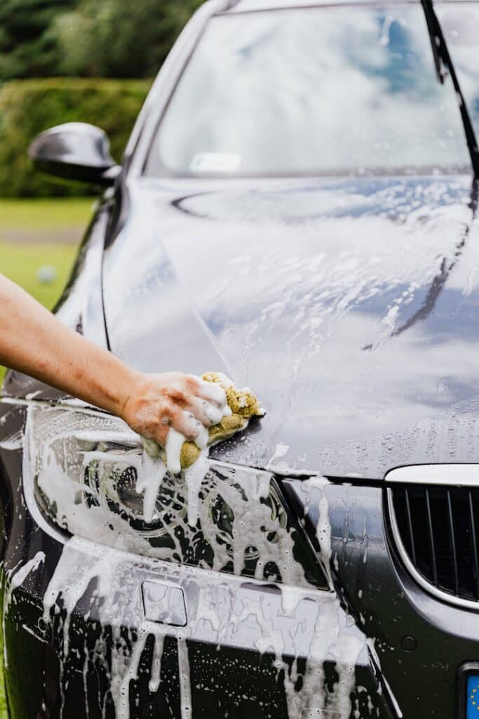A person diligently washes a car using a foam sponge, creating a bubbly lather on the vehicle's surface.