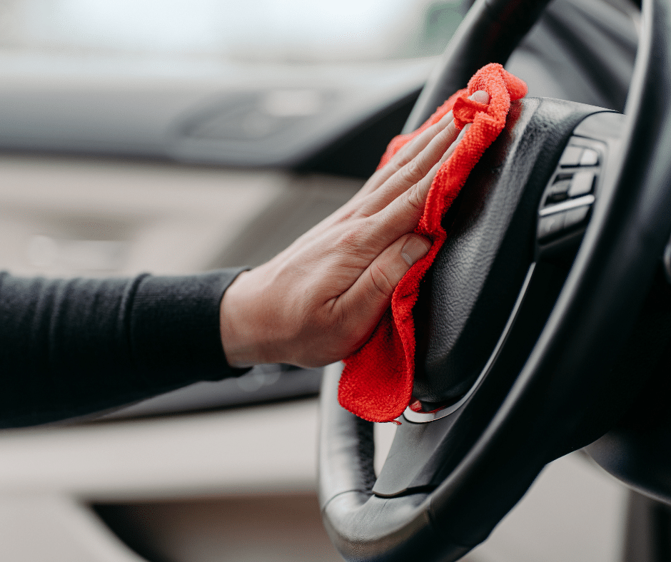 A person diligently cleaning the steering wheel of a car, ensuring a spotless and hygienic driving environment.