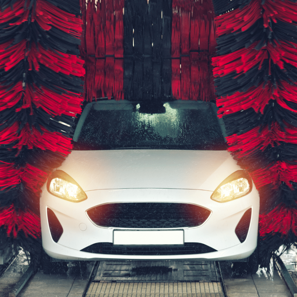 A car is being thoroughly cleaned at a car wash, with water and soap spraying over its surface.