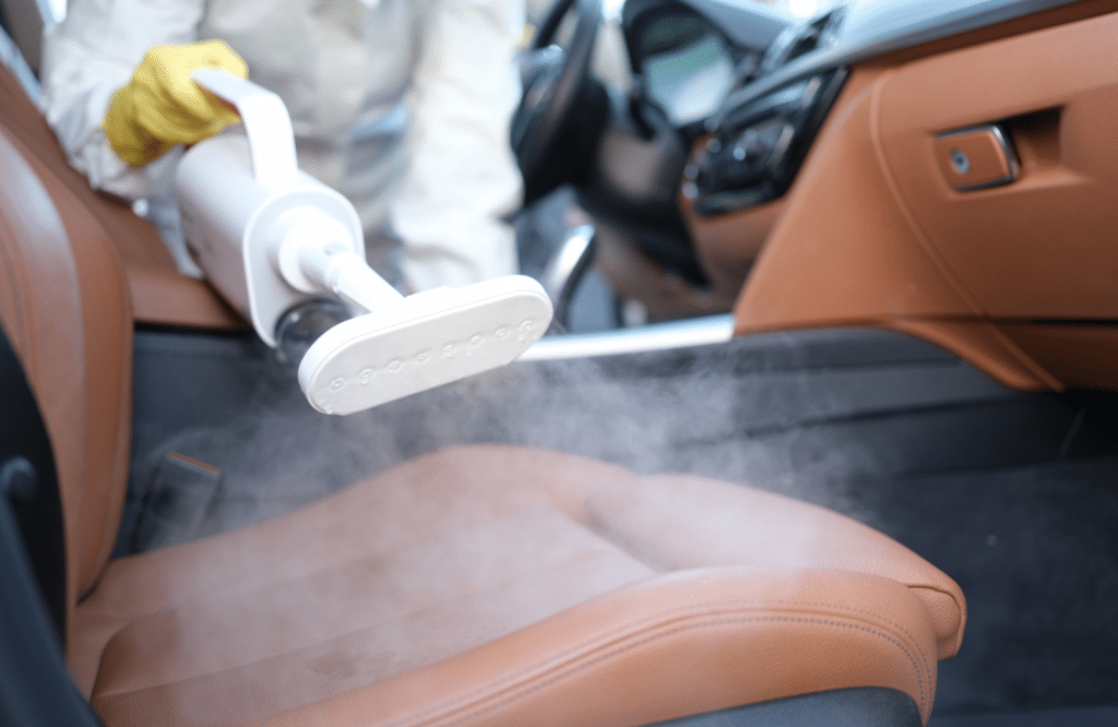 A person operates a steam cleaner to effectively clean the leather interior of a car.